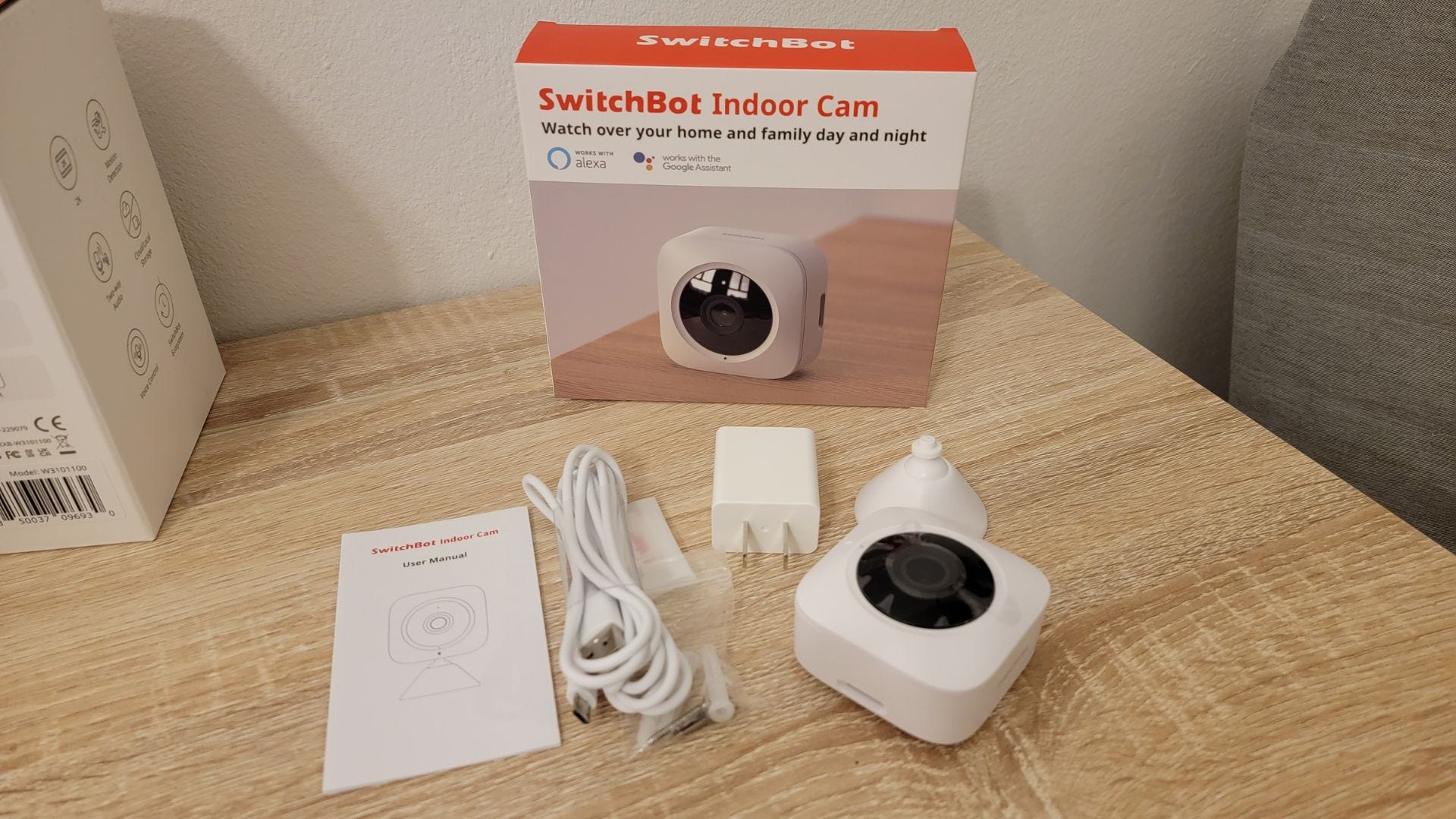 SwitchBot Indoor Security camera box and contents sitting on wood desk