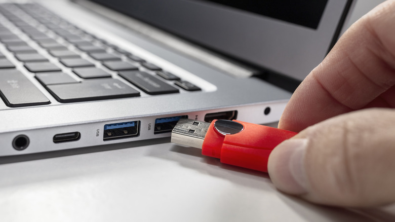 An individual connecting a USB flash drive to a laptop