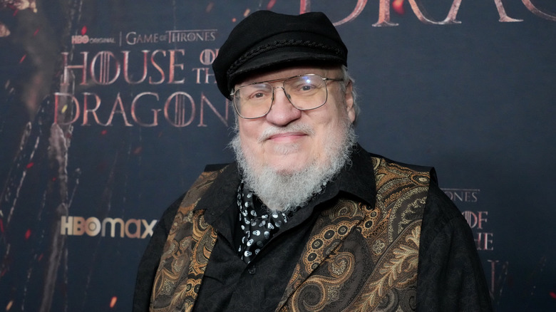 George RR Martin stands in front of a poster for the new Game of Thrones television series, House of the Dragon.