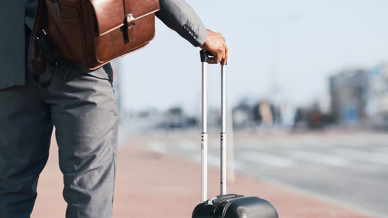 A man's back on the street holding a suitcase.