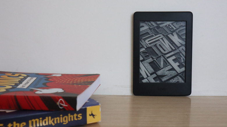 Kindle reader placed on a table beside books