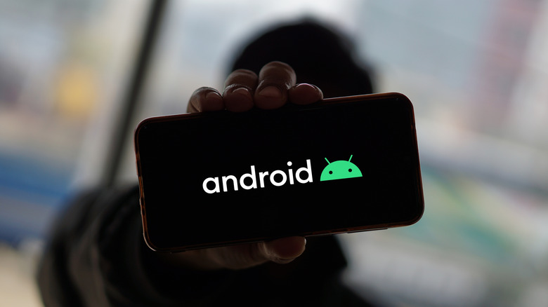 A person displaying a phone featuring the Android logo on its display