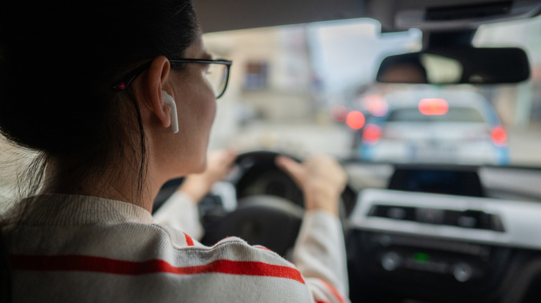A side view of a woman driving while wearing an earbud.
