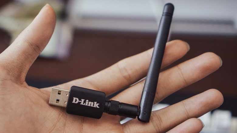 A person's hand holding a USB Wi-Fi dongle with an antenna