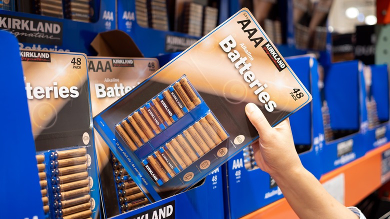 A hand taking Kirkland batteries out of a package in a store.