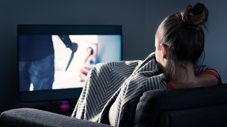 A woman watching a horror movie on TV.