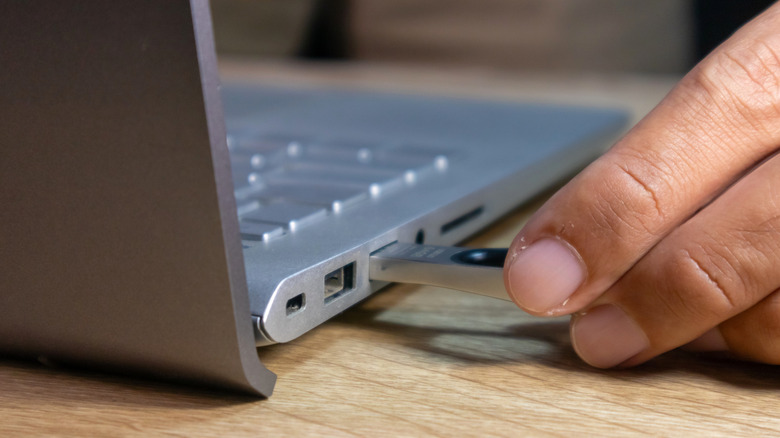 individual inserting a flash drive into a laptop's USB port