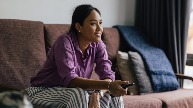 A woman smiling on the couch while holding a TV remote.