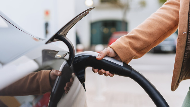 Close-up of an individual connecting an electric vehicle to a charging station.