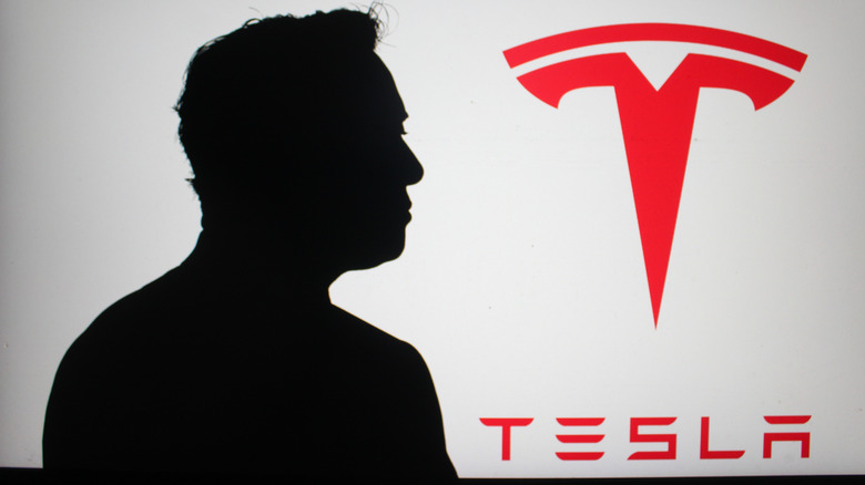 Elon Musk's silhouette discernible against the Tesla company logo.