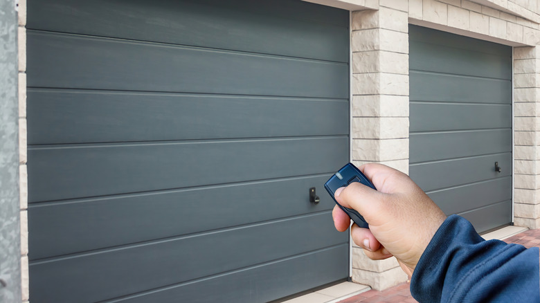 A person using a remote control in front of a garage door.