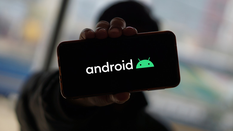 A person holding out a phone that shows the Android logo on its screen.