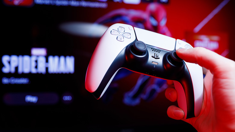 Close up of one hand holding a PS5 controller with Marvel's Spider-Man on the home screen in the background.
