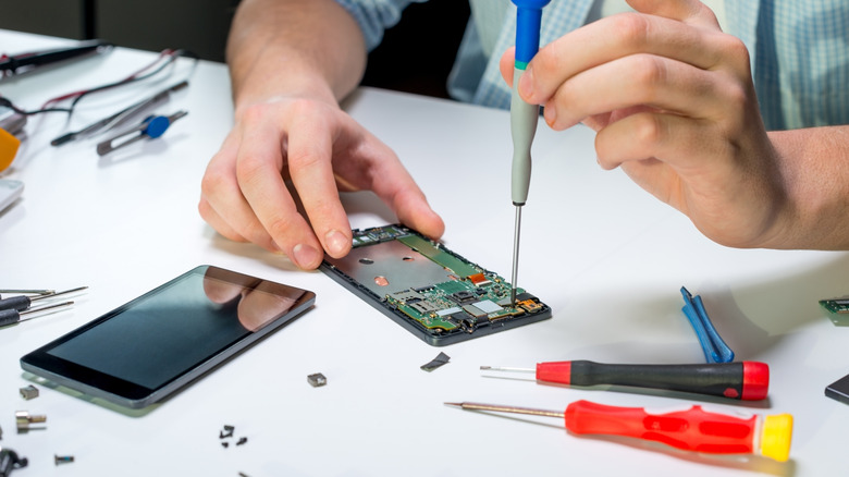 A disassembled phone on a table with a person using a screwdriver to unscrew a component on the motherboard