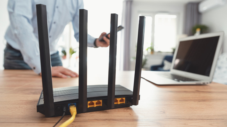 router located on a wooden table next to a laptop with a person in the background