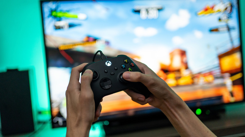 Hands holding an Xbox controller in front of a blurred out TV