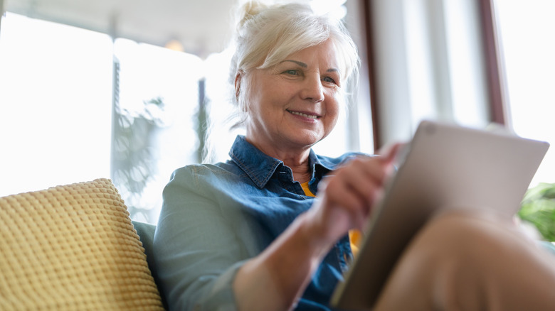 woman interacting with a digital tablet while seated on a couch at home